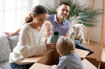 Happy Family With Kids Unpacking Boxes Moving Into New Home (1)